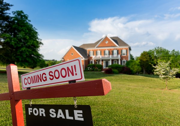 A Coming Soon and For Sale sign on the lawn in front of a brick house